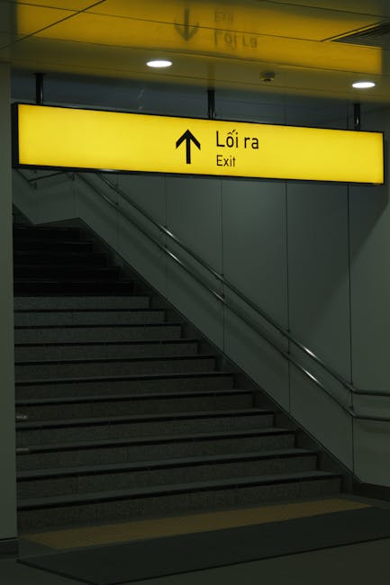Inside a building at the top of a stairwell, the image shows a clear view of a level entrance to a train station, specifically Waterloo Station, with a focus on the ticket barriers. The downward persp